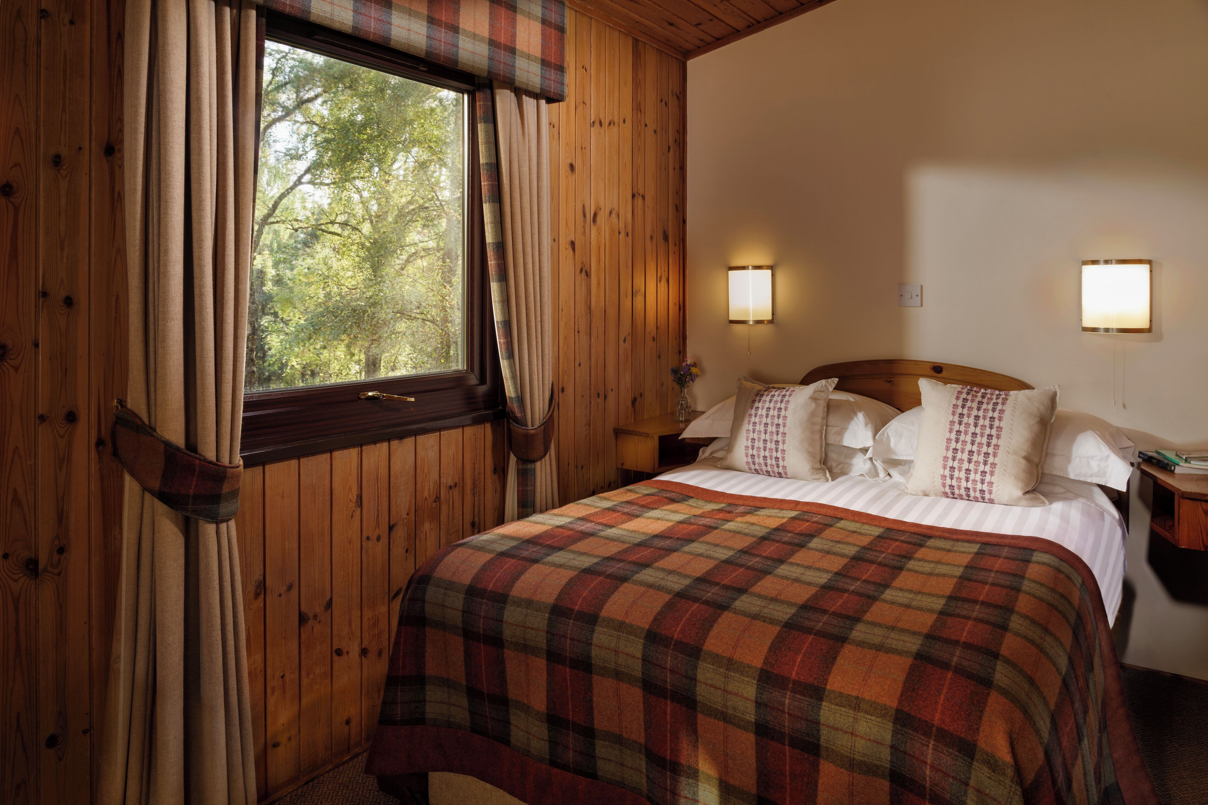 Ein Zimmer mit Holzwänden, einem Bett, zwei Nachttischen und einem fenster mit Vorhängen.