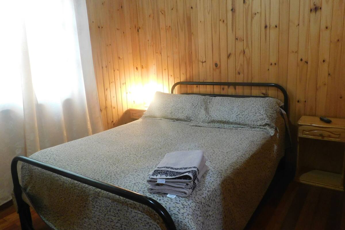 A single bed with a patterned bedspread, a folded towel, and a nightstand with a remote control.