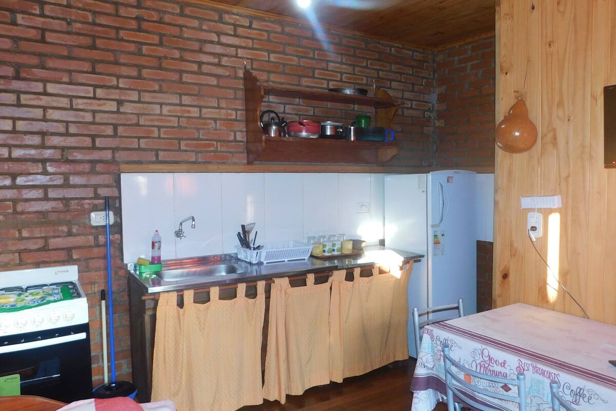 A compact kitchen with a brick wall, a wooden countertop, and a refrigerator.