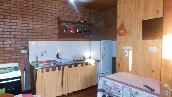A compact kitchen with a brick wall, a wooden countertop, and a refrigerator.