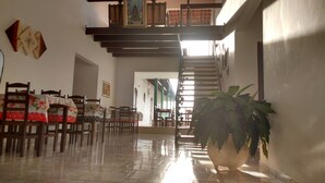 Une pièce spacieuse dotée d’un sol carrelé, de chaises en bois, d’une grande plante en pot et d’un escalier menant à un niveau supérieur.