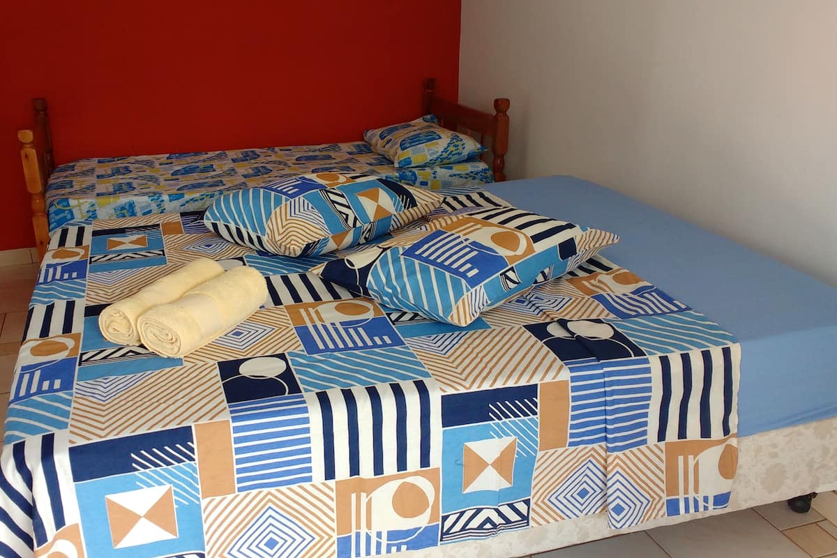 Una cama con colcha estampada y almohadas, cabecero de madera y pared roja.