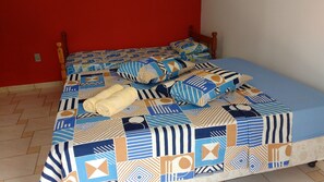 A bed with a patterned bedspread and pillows, a wooden headboard, and a red wall.