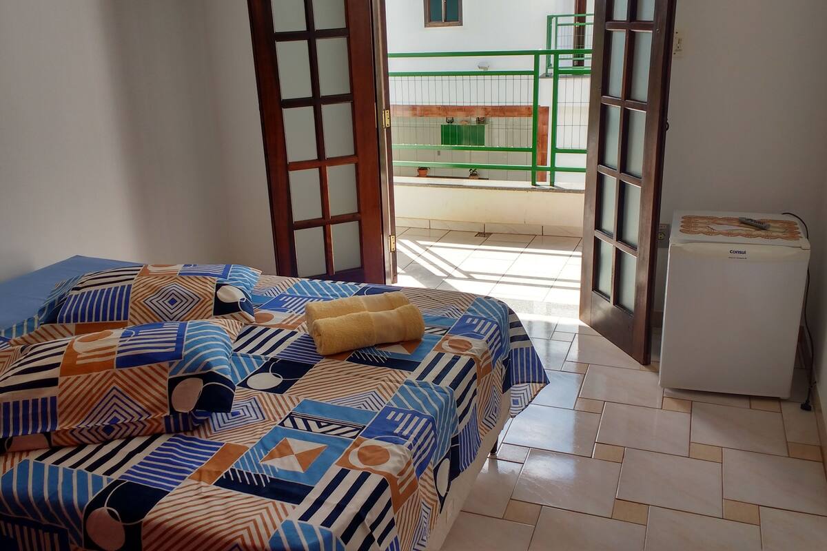 Un dormitorio con una colcha estampada, una mesita de noche pequeña y un equipo de aire acondicionado blanco.