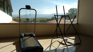 Une pièce équipée d’un tapis de course, d’un vélo d’appartement et offrant une vue sur des collines lointaines grâce à une grande fenêtre.