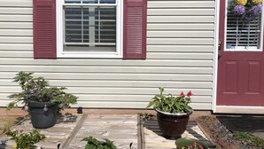 A house with a red door, a window with white shutters, and several potted plants on the porch. - Bluewaters Retreat Bachelor Unit (Earnscliffe)