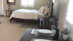 A bedroom with a bed, a bedside table, a mirror, and a window. - Bluewaters Retreat Bachelor Unit (Earnscliffe)