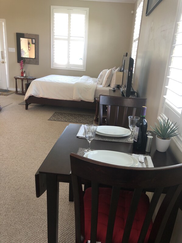 A bedroom with a bed, a bedside table, a mirror, and a window. - Bluewaters Retreat Bachelor Unit (Earnscliffe)