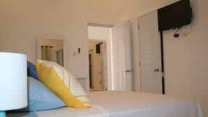 A bedroom with two beds, a bedside table with a lamp, and a television mounted on the wall. - Villas Michaela Caribean (Cabarete)