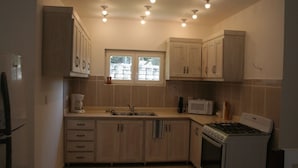 A compact kitchen with wooden cabinets, a built-in microwave, a gas stove, and a window with a view of the outside. - Villas Michaela Caribean (Cabarete)