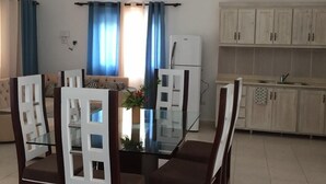 A modern kitchen with white cabinets and a dining area with a glass table and wooden chairs. - Villas Michaela Caribean (Cabarete)