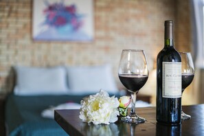 Una botella de vino y dos copas sobre una mesa, con una flor y una cama al fondo.