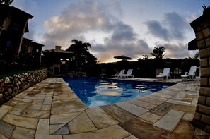Una piscina con baldosas de piedra y sillones blancos para tomar el sol.