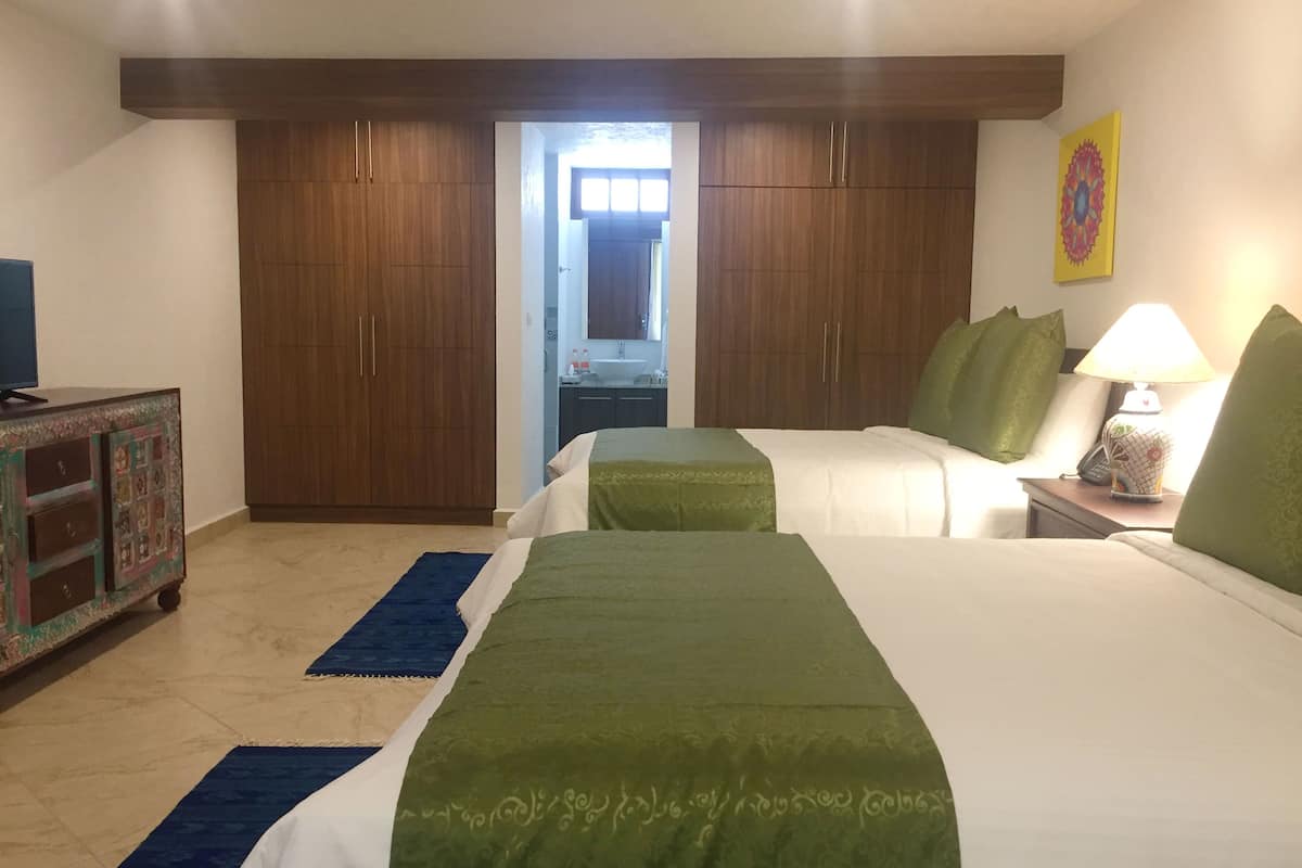 A hotel room with two beds, a desk with a lamp, a dresser, and a large wardrobe.