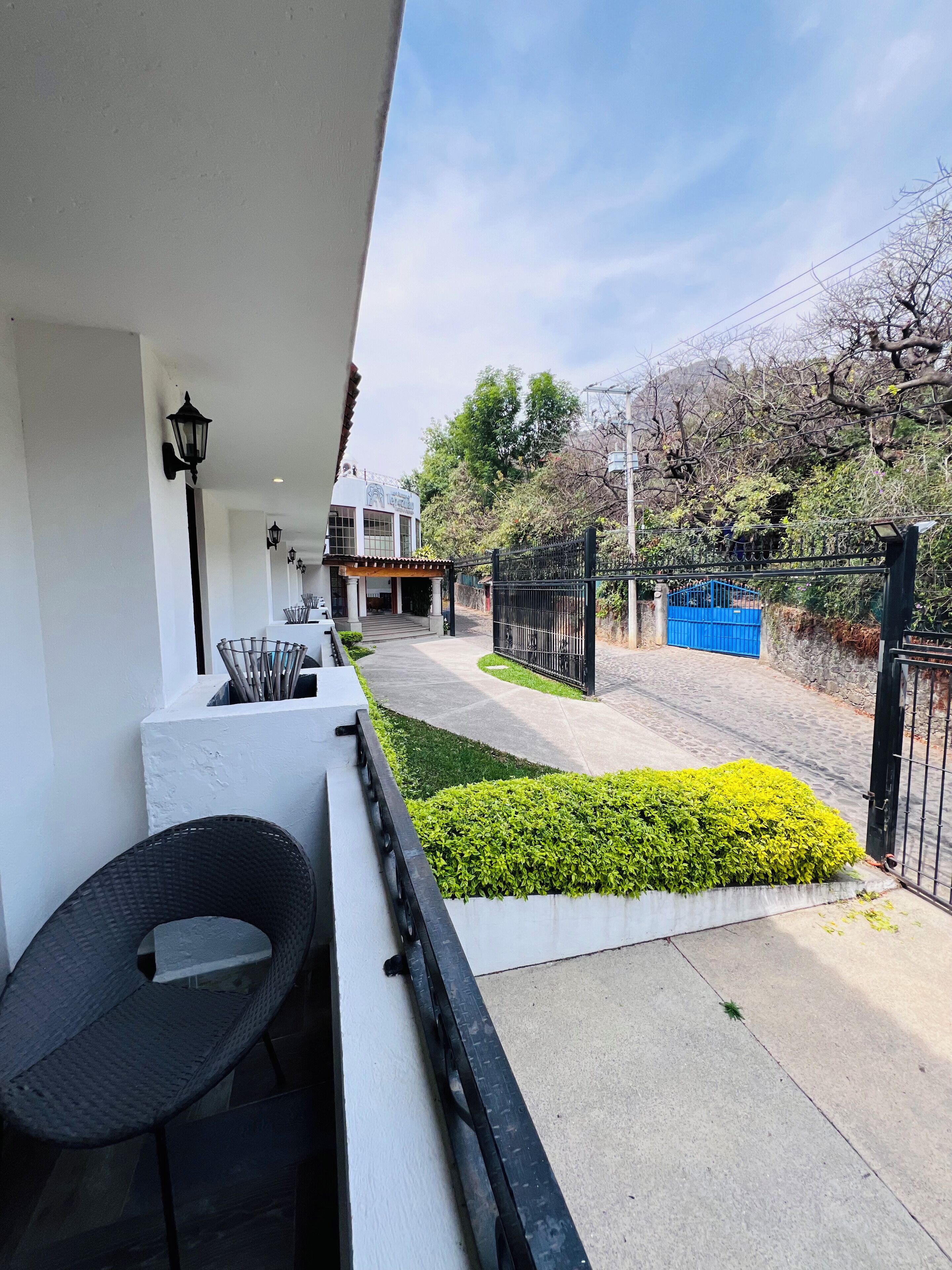 A balcony with a view of a building, a paved pathway, and a blue gate.