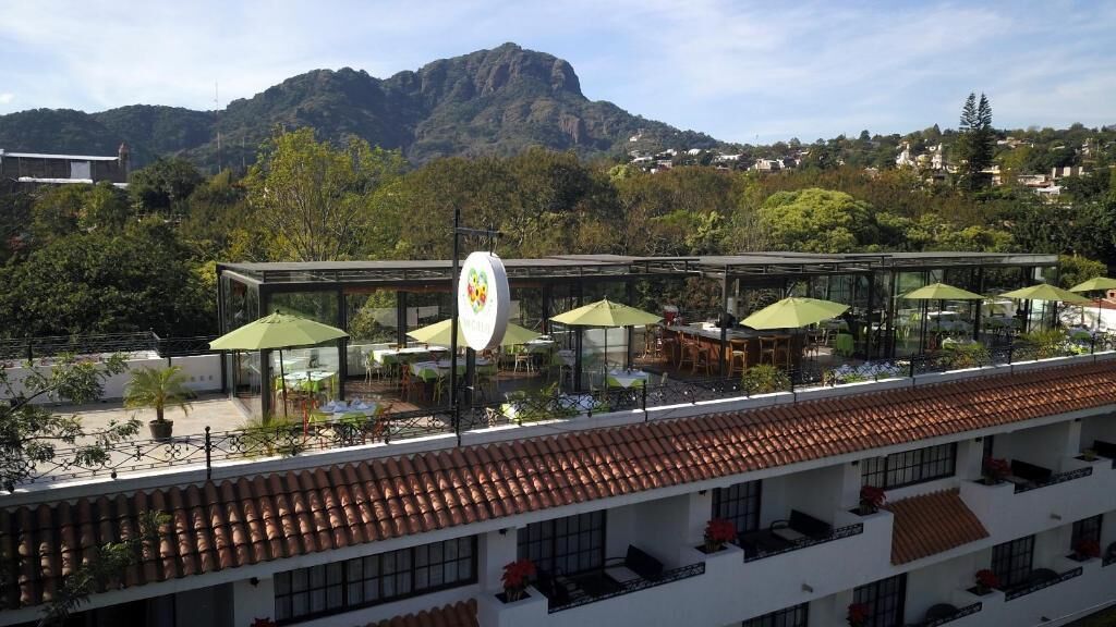 A hotel with outdoor seating, a mountain view, and a white building with red-tiled roofs.