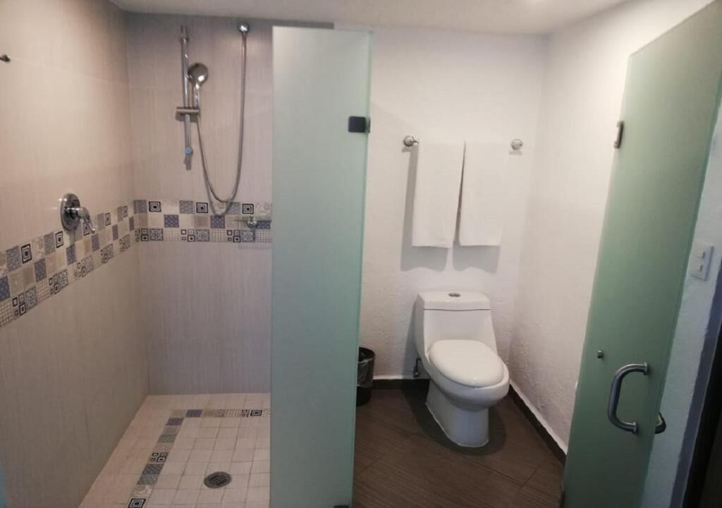 A bathroom with a shower, toilet, and tiled floor.