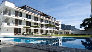 Un hotel moderno con piscina, mobiliario exterior y vistas a las montañas.