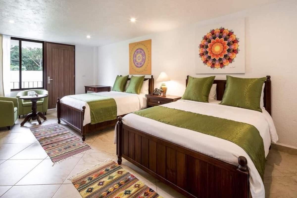A hotel room with two beds, a small table, a chair, and a large window.
