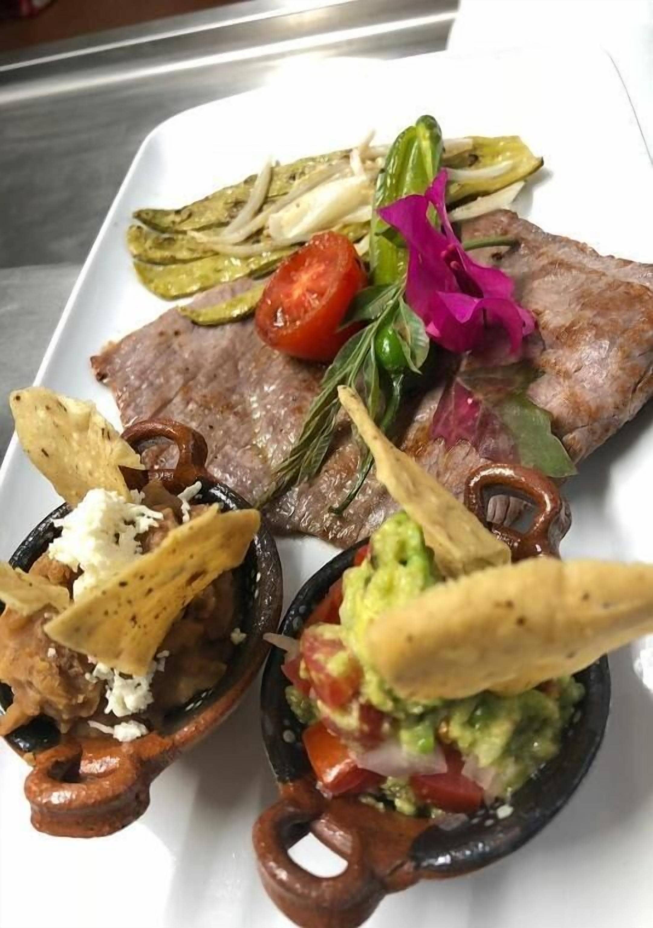 A plate of food with a steak, grilled vegetables, and a side of guacamole.