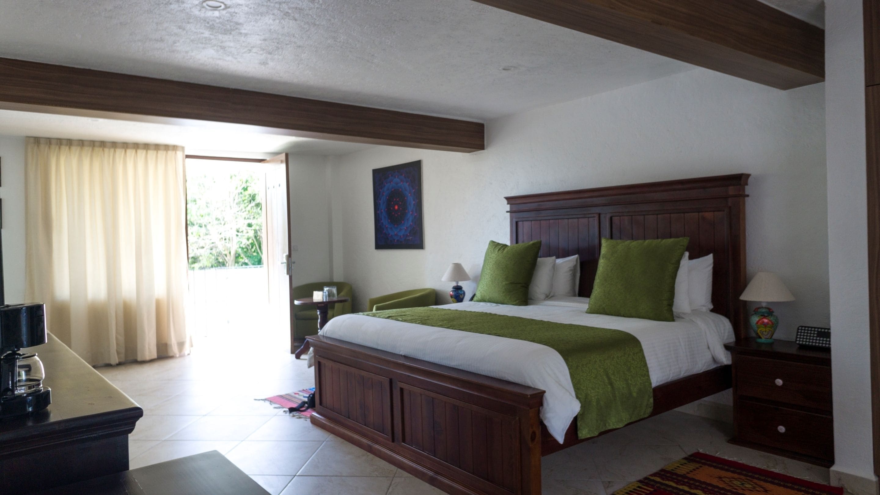 Un dormitorio con una cama de madera, almohadas verdes, una mesita de noche, una lámpara y un cuadro en la pared.