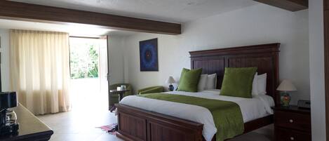 Un dormitorio con una cama de madera, almohadas verdes, una mesita de noche, una lámpara y un cuadro en la pared.
