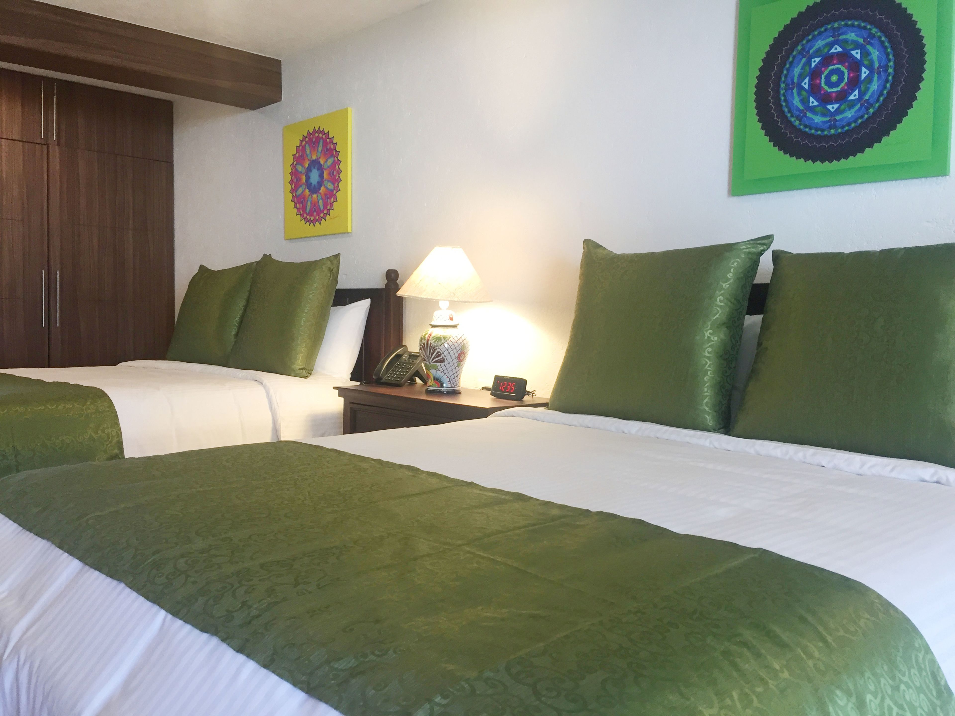 A hotel room with two beds, green bedding, a nightstand with a lamp, a phone, and a clock displaying 12:35.