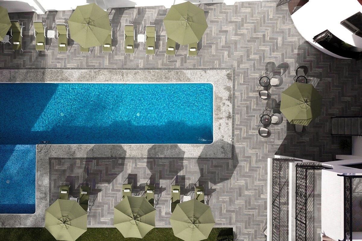 Una piscina en la azotea con suelo de dibujo de espiga, rodeada de sillones de descanso y sombrillas.