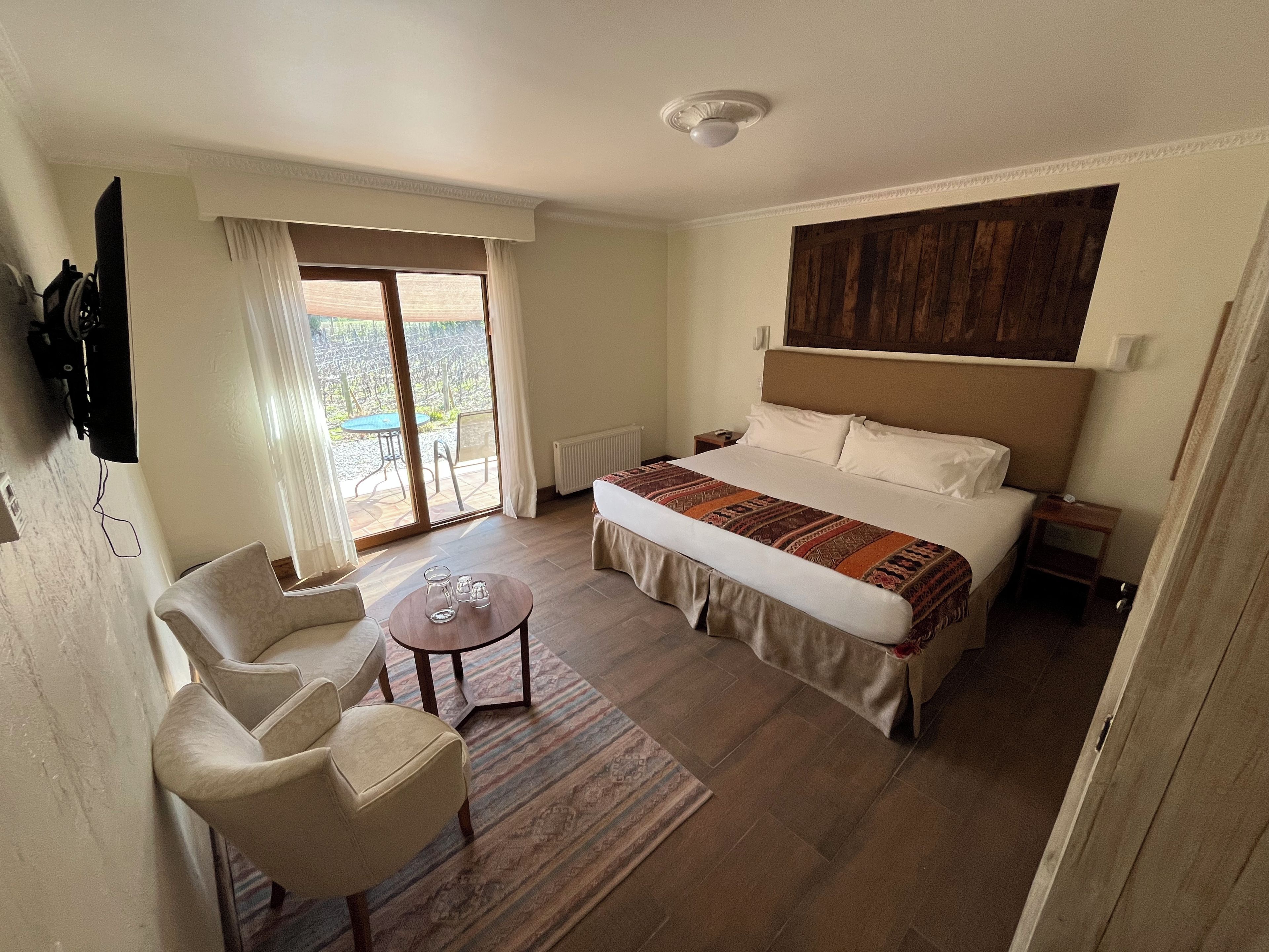 A hotel room with a bed, a desk, a chair, a TV, and a sliding glass door to the outside.