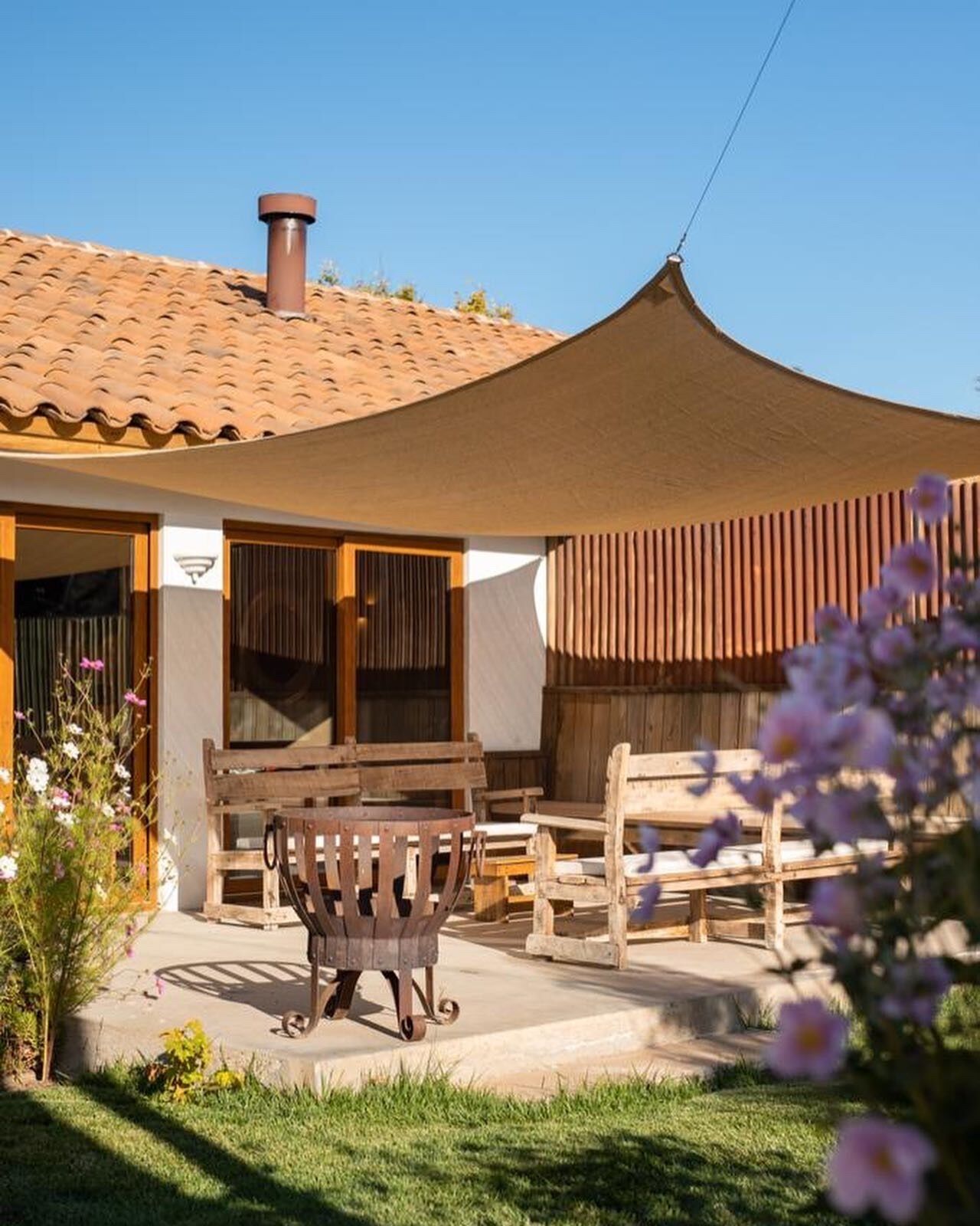 Una casa rústica con techo de tejas, un porche cubierto con muebles de madera y un jardín lleno de flores.