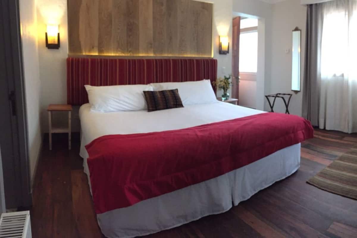 Une chambre d’hôtel avec un grand lit, une tête de lit en bois, une petite table, une chaise et un miroir.