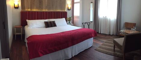 A hotel room with a large bed, a wooden headboard, a small table, a chair, and a mirror.
