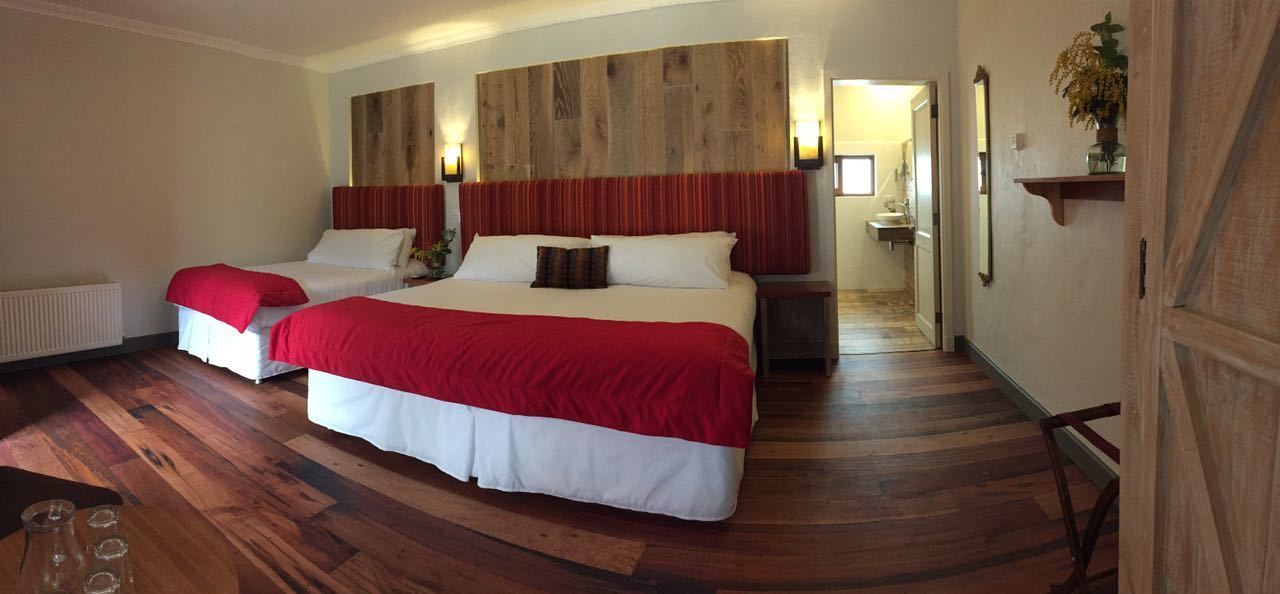 Habitació d'hotel amb un llit gran, dos llits més petits, sòl de fusta, un capçal de llit de fusta i un passadís que condueix a un bany.
