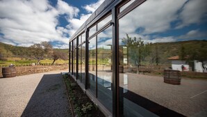 Un edificio moderno con ampie vetrate, un vialetto ghiaioso e un paesaggio rurale sullo sfondo, con alberi e colline.