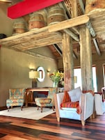 Un interior rústico con vigas de madera, chimenea, sillones estampados y un sofá.