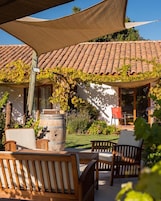 Un patio con muebles de madera, un barril y una pérgola cubierta de hiedra.