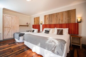 Habitación de hotel con dos camas, cabeceros de madera, un armario de madera y una mesita de noche con lámpara.