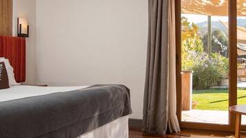 Un dormitorio con una cama grande, piso de madera, vista a un jardín por una puerta de cristal y una mesita.