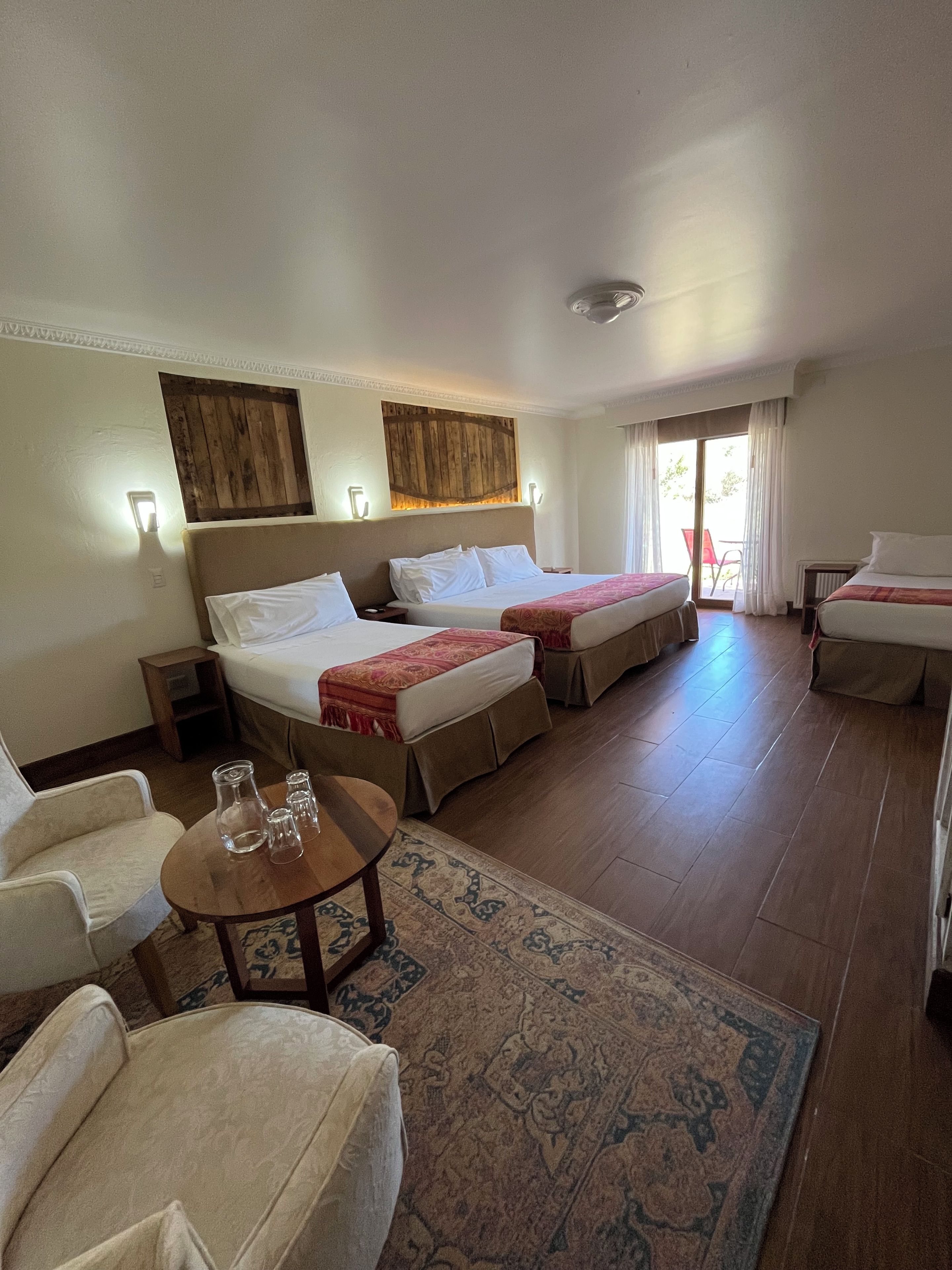 A hotel room with two beds, a sofa, a small table with glasses, and a patterned rug.