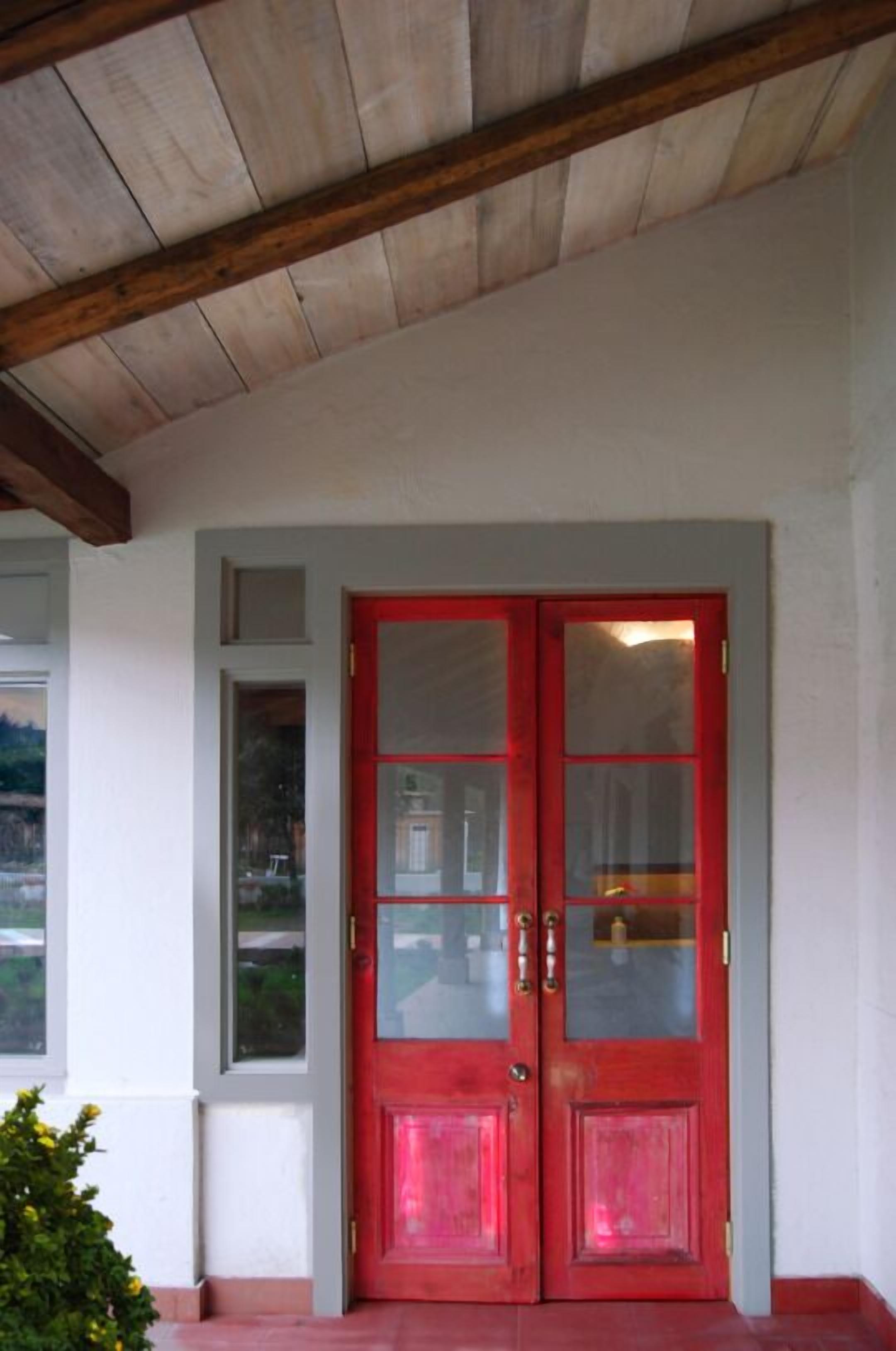 Una puerta doble roja con paneles de vidrio, techo de madera y una pequeña ventana a la izquierda.
