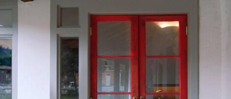 Una puerta doble roja con paneles de vidrio, techo de madera y una pequeña ventana a la izquierda.