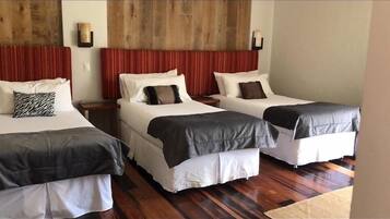 A hotel room with two single beds, each with a headboard, a nightstand, and a lamp. The room has wooden flooring and a large window.