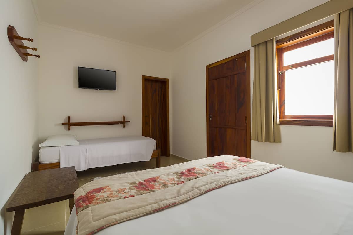 Une chambre à coucher comprenant un lit, une table de chevet, un téléviseur fixé au mur et une fenêtre avec des rideaux.