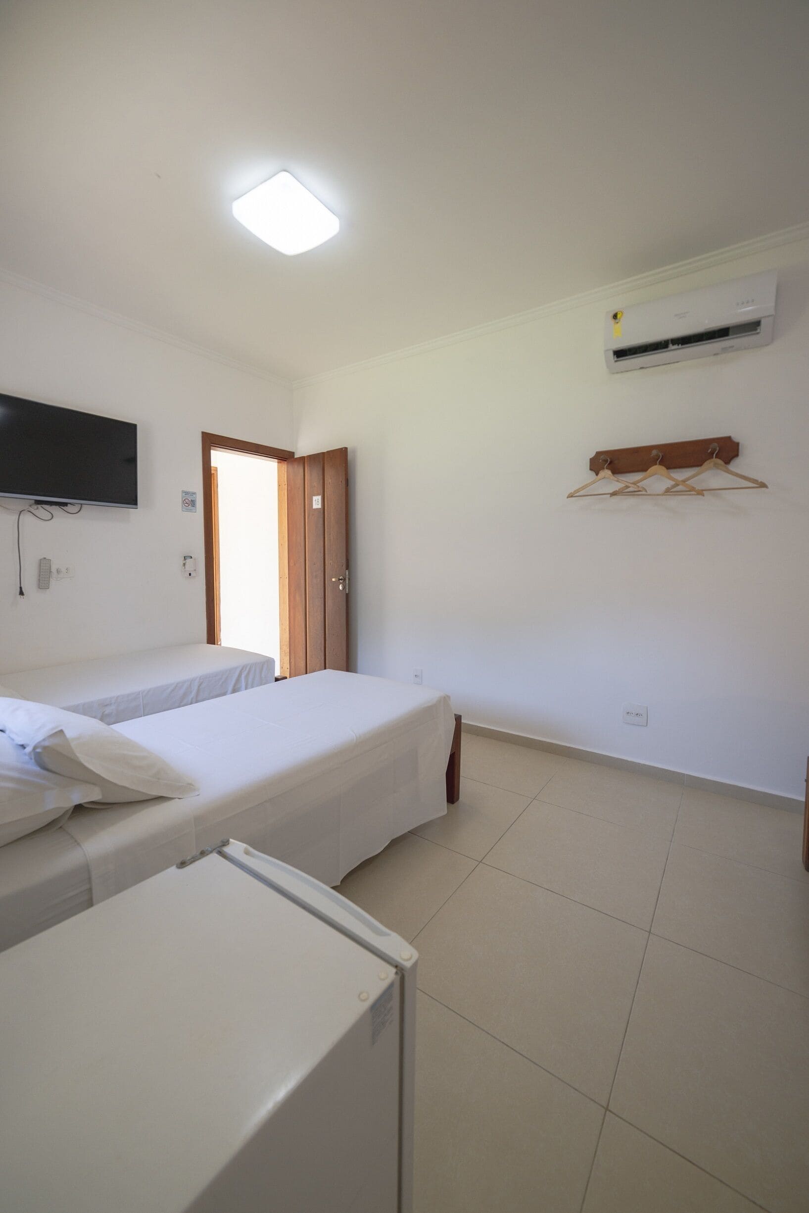 A room with two beds, a television mounted on the wall, an air conditioning unit, and a wooden door.