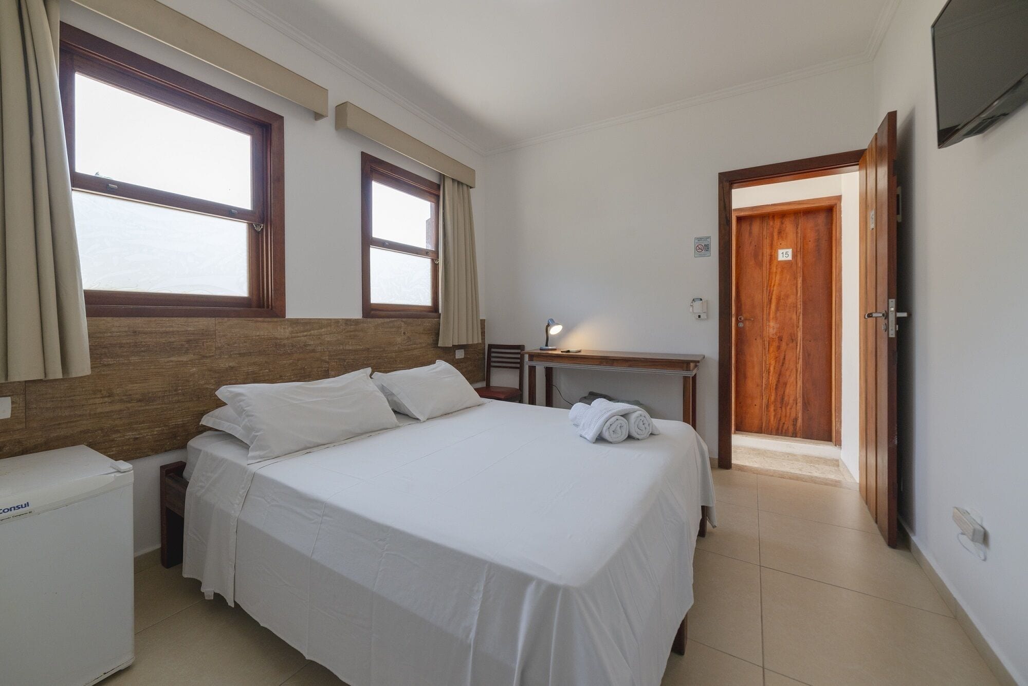 A hotel room with a bed, a desk, a chair, a TV, and a door.