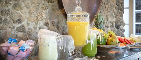 Un tavolo da buffet con diversi cibi e bevande, tra cui una brocca grande di succo d'arancia, una caraffa di bevanda verde e una ciotola di frutta.
