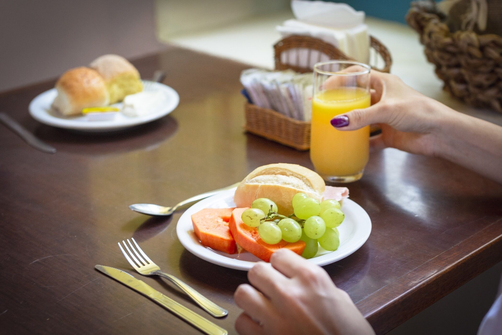 A dining table with plates of food, utensils, and a glass of orange juice.