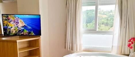 Une pièce avec une télévision, une baignoire remplie de pétales de roses, un seau avec une bouteille et une fenêtre avec des rideaux.