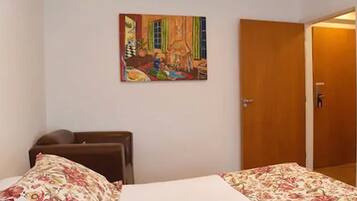 Una habitación de hotel con una cama, una puerta de madera y un cuadro llamativo en la pared.