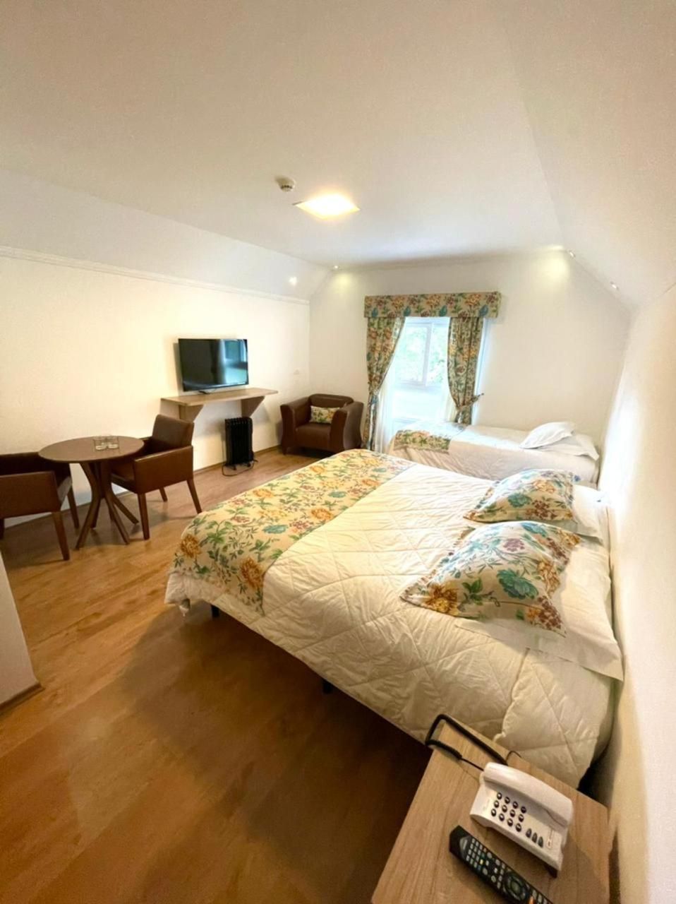 A hotel room with a bed, a desk, a chair, a TV, and a window with curtains.